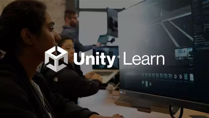 Logo de Unity Learn superposé à des développeurs travaillant sur un projet de jeu vidéo face à leurs écrans